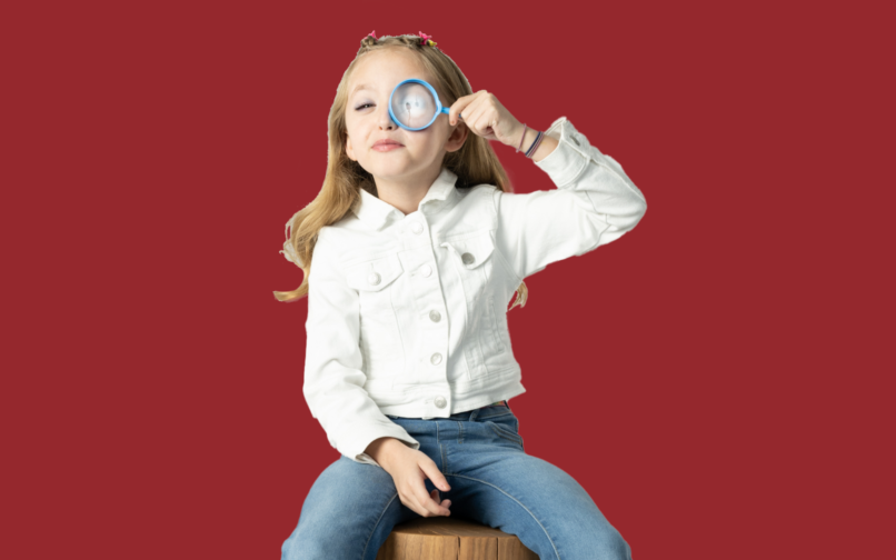 Girl holding magnifying glass in front of red background